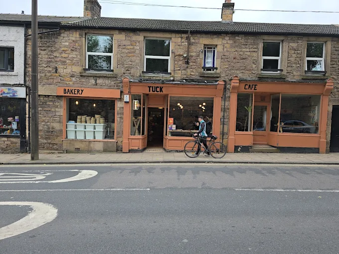 Street view of Tuck Bakery and Café in a traditional stone building, offering freshly baked goods and local produce in Lancaster, with a cyclist passing by.